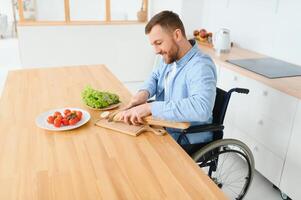 Jeune désactivée homme séance sur roue chaise en train de préparer nourriture dans cuisine photo