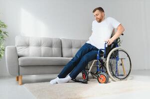 désactivée homme à Accueil essaie à avoir à le sien pieds dans une fauteuil roulant. le concept de réhabilitation après blessures et voiture les accidents. photo