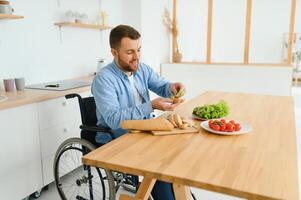 Jeune désactivée homme séance sur roue chaise en train de préparer nourriture dans cuisine photo