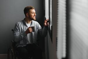 Jeune désactivée homme séance dans une fauteuil roulant près le fenêtre photo