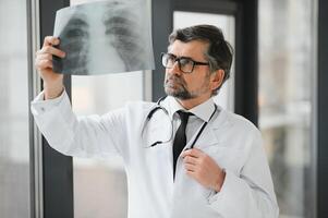 une Sénior médecin à la recherche à le radiographie dans le sien bureau. photo