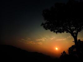 le Soleil réglage derrière une arbre dans le montagnes photo