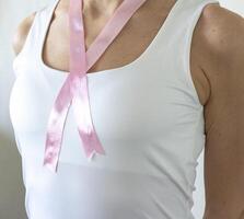 coup de le femme dans le blanc Haut contre le blanc mur, avec rose ruban sur sa cou comme une symbole de Sein cancer conscience. concept photo