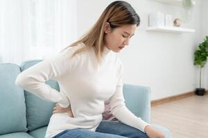 Asie magnifique femme en portant sa inférieur retour tandis que et souffrir de insupportable douleur santé et problèmes, chronique retour douleur, mal au dos dans Bureau syndrome, scoliose, hernie disque, muscle inflammation photo