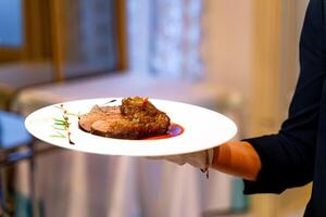 une la personne en portant une assiette avec une pièce de Viande. une la personne en portant une assiette avec une pièce de Viande sur il photo