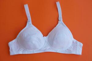 blanc soutien-gorge sur Orange arrière-plan.concept, féminin soutien-gorge. classique confortable avec tasse une pour femelle Jeune adolescents. protéger et tenir magnifique seins. Sein cancer conscience. photo