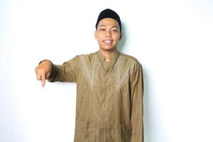 souriant asiatique musulman homme montrer du doigt vers le bas portant islamique robe isolé sur blanc Contexte photo