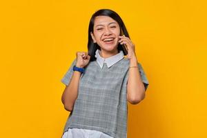 joyeuse jeune femme asiatique recevant un appel entrant sur smartphone et regardant de côté sur fond jaune photo