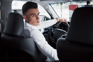 un jeune homme est assis dans une voiture nouvellement achetée au volant, un achat réussi. photo