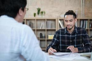 présentation des jeunes startups en réunion. le travailleur occasionnel parle avec un client asiatique de la réussite d'un projet financier. confiant dans la planification des affaires, sur le bureau d'un petit bureau. photo