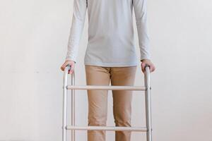 tondu vue de personnes âgées homme en marchant avec Cadre à maison, fermer. Jeune Masculin asiatique en utilisant médical équipement à bouge toi autour le sien maison. désactivée plus âgée la personne dans avoir besoin de professionnel Aidez-moi photo