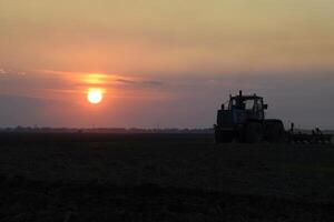 tracteur labour charrue le champ sur une Contexte le coucher du soleil. tracteur silhouette sur le coucher du soleil Contexte photo