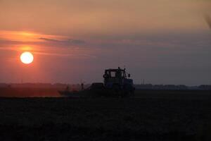 tracteur labour charrue le champ sur une Contexte le coucher du soleil. tracteur silhouette sur le coucher du soleil Contexte photo