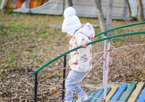 peu fille est en jouant sur le terrain de jeux dans le parc. le enfant va sur le pas de le Cour de récréation. photo