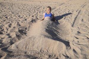 fille dans une bikini sur le plage enterré dans moitié dans le sable. photo