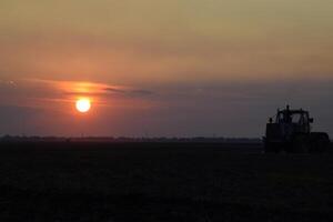 tracteur labour charrue le champ sur une Contexte le coucher du soleil. tracteur silhouette sur le coucher du soleil Contexte photo