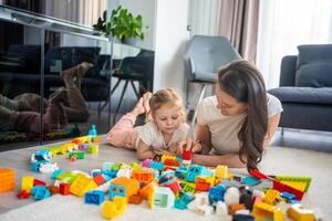 peu fille jouer avec constructeur jouet sur sol dans Accueil avec maman ou femme Baby-sitter, éducatif jeu, famille à Accueil dépenser loisir Activités temps ensemble concept photo