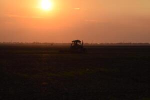 tracteur labour charrue le champ sur une Contexte le coucher du soleil. tracteur silhouette sur le coucher du soleil Contexte photo