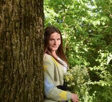 Jeune magnifique femme est permanent dans le forêt avec une bouquet de camomille photo
