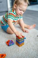 peu fille en jouant coloré aimant Plastique blocs trousse à maison. le enfant en jouant éducatif Jeux. de bonne heure enfance développement. photo