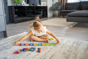 peu fille en jouant coloré aimant Plastique blocs trousse à maison. le enfant en jouant éducatif Jeux. de bonne heure enfance développement. photo