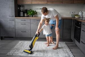 père et fille ayant amusement avec vide nettoyeur tandis que nettoyage à Accueil cuisine photo