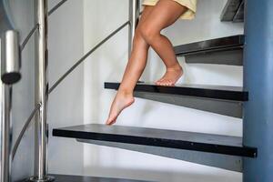 proche en haut vue de peu enfant fille pieds Aller vers le bas le escaliers à maison, enfant escalade spirale escalier photo