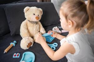 peu fille en jouant médecin avec jouets et nounours ours sur le canapé dans vivant pièce à Accueil photo