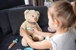 peu fille en jouant médecin avec jouets et nounours ours sur le canapé dans vivant pièce à Accueil photo