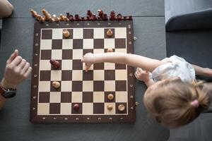 père enseignement le sien peu fille à jouer échecs à le table dans Accueil cuisine. le concept de bonne heure enfance développement et éducation. famille loisirs, la communication et des loisirs. photo