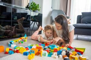 peu fille jouer avec constructeur jouet sur sol dans Accueil avec maman ou femme Baby-sitter, éducatif jeu, famille à Accueil dépenser loisir Activités temps ensemble concept photo