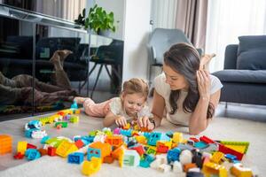 peu fille jouer avec constructeur jouet sur sol dans Accueil avec maman ou femme Baby-sitter, éducatif jeu, famille à Accueil dépenser loisir Activités temps ensemble concept photo