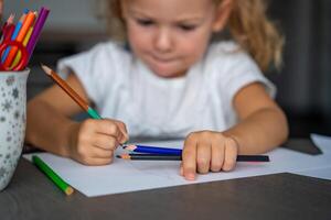 peu fille dessine avec coloré des crayons dans maison. photo