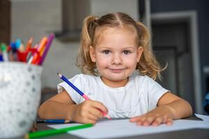 peu fille dessine avec coloré des crayons dans maison. photo