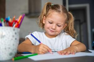 peu fille dessine avec coloré des crayons dans maison. photo