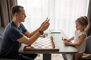 père enseignement le sien peu fille à jouer échecs à le table dans Accueil cuisine. le concept de bonne heure enfance développement et éducation. famille loisirs, la communication et des loisirs. photo