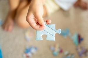 puzzle pièce dans enfant main. peu fille est assis à Accueil sur le tapis et recueille puzzles photo