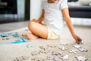 peu blond fille est assis à Accueil sur le tapis et recueille énigmes. concentrer sur le puzzle pièces photo