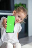 peu fille est séance et en portant une téléphone intelligent avec une chromakey photo