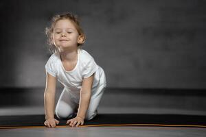 peu mignonne fille pratiquant yoga pose sur gris Contexte dans foncé chambre. haute qualité photo