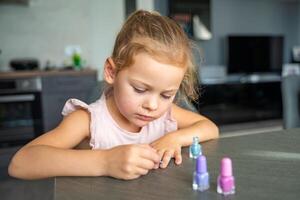 peu fille Faire manucure et La peinture ongles avec coloré rose, bleu et violet clou polonais à maison. photo