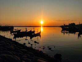 le coucher du soleil sur paiton plage avec silhouettes de pêche bateaux ancré dans le port photo