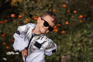 une peu garçon dans un astronaute costume pièces à l'extérieur entouré par fleurs sur une ensoleillé journée photo