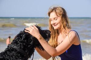blond fille avec une noir frisé chien sur le plage photo
