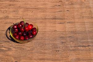 baies de une sucré Cerise dans une verre bol sur une en bois Contexte. mûr rouge sucré Cerise photo