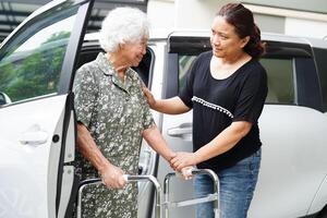 le soignant aide une patiente asiatique âgée handicapée à monter dans sa voiture, concept médical. photo