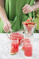 une femme dans une vert robe verse une rouge rafraîchissant boisson de le pastèque photo