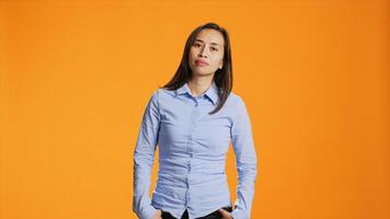 Jeune souriant femme permanent plus de Orange arrière-plan, sentiment sur de soi et insouciant dans studio. Naturel philippin la personne posant avec élégant vêtements sur caméra, jolie femelle modèle. photo