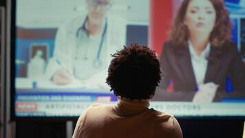 homme en train de regarder médical ai nouvelles discuté par présentateur, affiché sur intelligent la télé dans néon allumé appartement. la personne Suivant nouvelles à propos artificiel intelligence sur vidéo sur demande canaliser, proche en haut coup photo