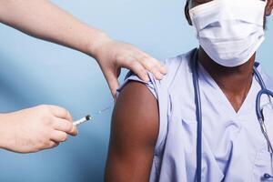 proche en haut de noir infirmière portant visage masque avoir vacciné avec seringue par caucasien personne. africain américain médical spécialiste recevoir vaccin coup de mains de médecin pour virus protection. photo